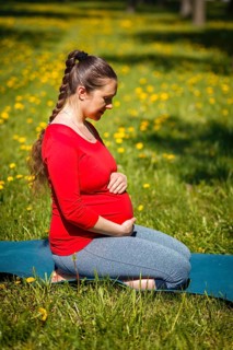Pregnancy yoga exercise, pregnant woman doing asana Virasana Hero Pose on knees outdoors on grass