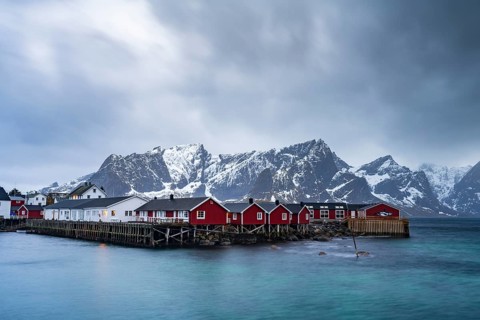 Rorbuer cabins of Hamnoy by the fjord, snowy mountains in the back, Hamnøy, Reine, Moskenesøya,