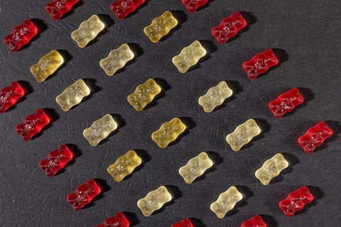 Different coloured gummy bears in rows, on a dark background