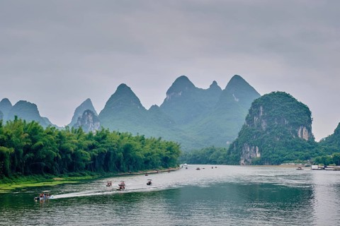 Tourist boats on Li river with dramatic karst mountain landscape in the background. Yangshuo,