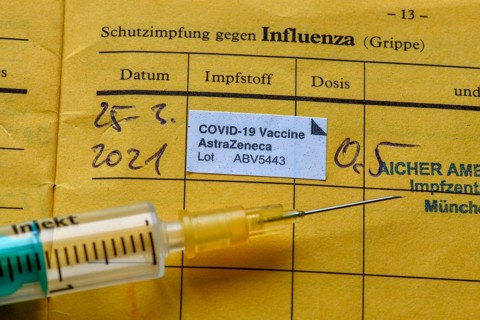 Syringe and vaccination certificate with entry for vaccination with AstraZeneca against Covid-19,