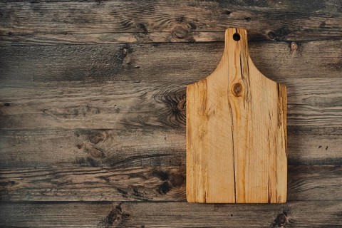 A wooden cutting board rests on a rustic wooden table, showcasing its natural grain and texture in