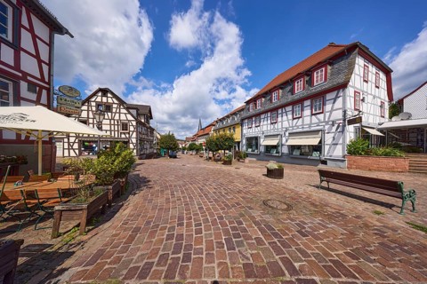 Brown street with half-timbered houses, benches and restaurant under blue sky with cumulus clouds