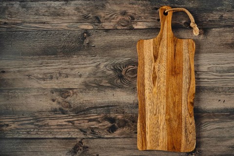 A handcrafted wooden cutting board rests on a weathered wooden table, displaying rich grains and