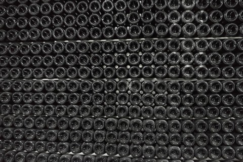Sparkling wine is aged in bottles in a dark cellar background