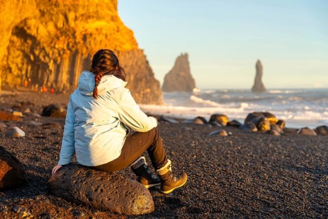 Female hiker sitting on the black sand beach of Reynisfjara looking at the sea. Iceland