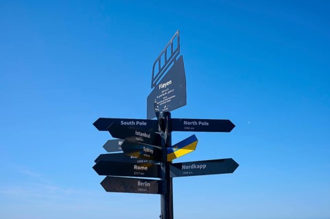 Black signpost against a blue sky with directions to various towns and destinations, Fløibanen