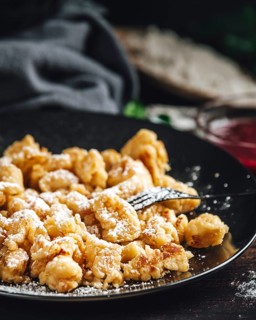 Close-up of Kaiserschmarrn on a black plate, dusted with sugar, jam in the background, dark