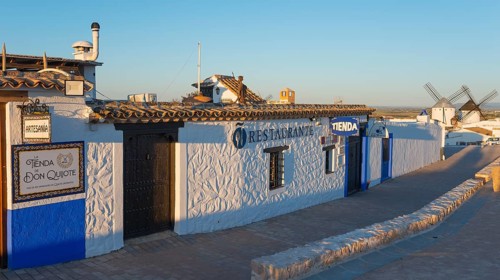 Building with white-blue walls and restaurant sign in a rustic landscape, windmills in the