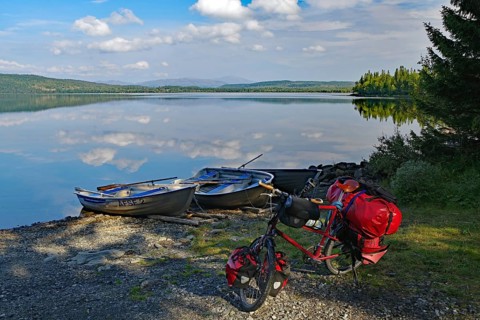 A lake with docked boats, a bicycle standing on the shore, surrounded by trees and under a cloudy