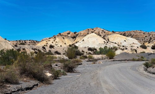 Dusty path through a dry, rocky desert landscape under a clear blue sky, Tabernas Desert, Desierto