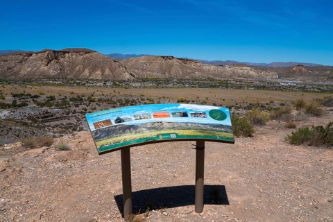 Viewpoint with an information board in a desert landscape with mountains and a clear sky, Llano de