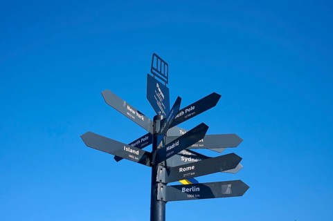 Black signpost against a blue sky with directions to various towns and destinations, Fløibanen
