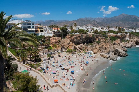 Well frequented beach with crystal clear water, many sunshades and people, surrounded by rocks and