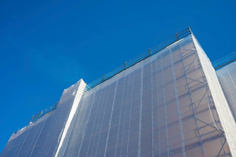 Shielding of a building by a tarpaulin attached to scaffolding against a clear blue sky, Bergen,