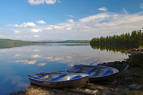 A calm lake with two docked boats, surrounded by trees and a slightly cloudy sky, Viken, Störlien,