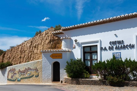 White building with restaurant and painted rock face, surrounded by shrubs and a sunny sky, Pedro