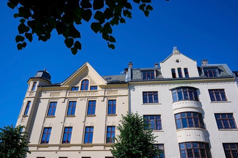 A historic building with an elaborate façade and many windows, surrounded by green trees under a