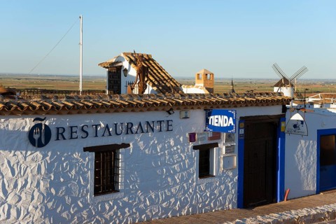 Rustic building with restaurant sign and white-blue walls, windmills in the background under a