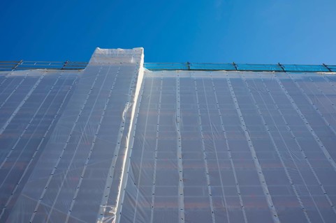 Shielding of a building by a tarpaulin attached to scaffolding against a clear blue sky, Bergen,