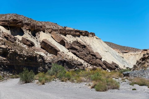 Rocks and cliffs rise in an arid desert landscape under a clear blue sky, La Tortuga, Tabernas