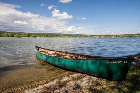 Green canoe on the shore of a lake with clear water and cloudy sky, quiet peaceful surroundings,