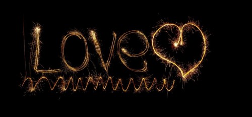Inscription Love and heart of sparklers. Sparks of holiday lights on black background with heart