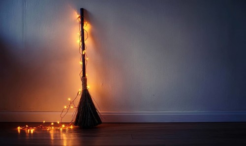 Simple witch's broom wrapped with warm orange fairy lights AI generated
