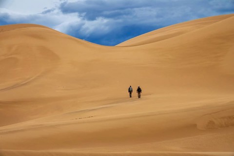 Two travelers in the desert. Hiking on sand dunes in mountains. Gobi desert, Mongolia, Asia