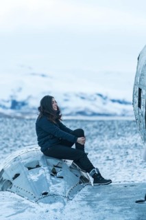 A woman sits on the engine of a crashed plane in the frozen Solheimasandur square in winter in