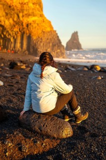 Female hiker sitting on the black sand beach of Reynisfjara looking at the sea. Iceland