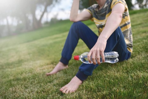 Young caucasian man runner relaxing holding drinking water bottle and sitting on grass in the park