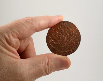 Old copper Russian coin of the 18th century hold between two fingers on neutral background