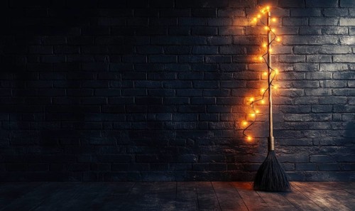 A minimalist witch's broom adorned with warm glowing garlands, against a simple brick wall AI