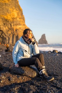 Portrait of a woman sitting on the black sand beach of Reynisfjara looking at the sea. Iceland