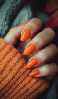 A close-up of a hand with vibrant orange nail polish and wearing a warm orange sweater creating a