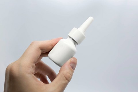 Young man is sick using nasal spray for blocked nose, spraying nose drops, hand holding nasal spray