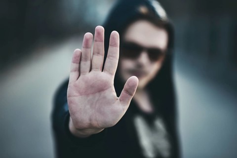 Portrait of fashion man in a black sweater with a hood and sunglasses, hand gestures