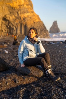 Portrait of female hiker sitting on Reynisfjara black sand beach looking at the sea. Iceland