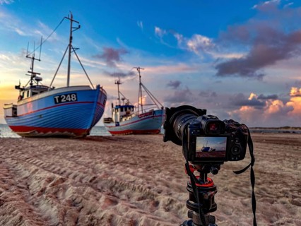 Tripod with camera in front of fishing boats on the beach in Vorupor, Denmark, Europe