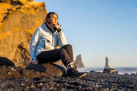 Portrait of pretty woman sitting on the black sand beach of Reynisfjara by the sea. Iceland