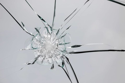 Broken window with cracks from impact or shot. Texture of cracks and chips on car windshield,