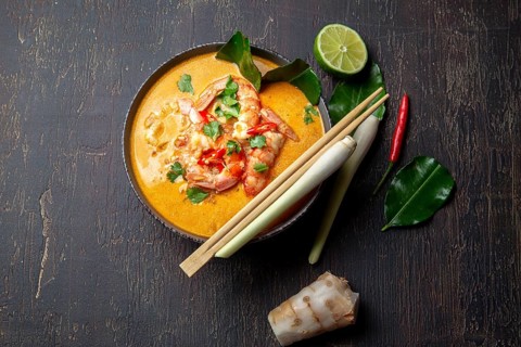 Shrimps Tom Yam Kung in grey bowl with thai spices on autentic tray top view, wooden background