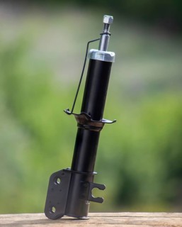 New shock absorber spare part car stands on a wooden board on a background of blurred green garden