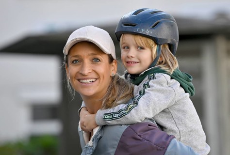 Mother, woman, blond, baseball cap, smiling, wearing boy with helmet, 5 years, blond, on shoulder,