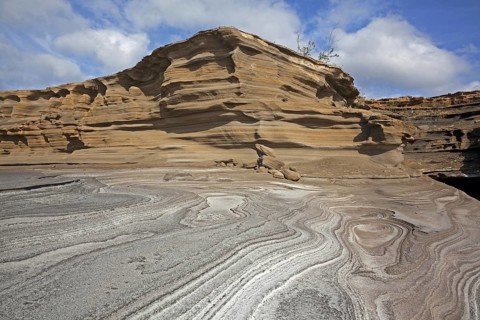 Pancake layered sandstone rock formations along the arid rocky coast on the island São Nicolau,