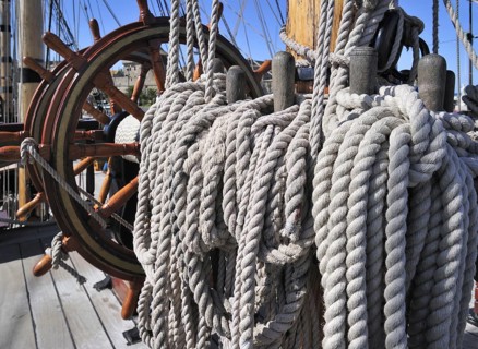 Steering wheel and ropes coiled around belaying pins aboard the Grand Turk, Etoile du Roy, a