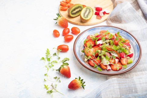 Vegetarian fruits and vegetables salad of strawberry, kiwi, tomatoes, microgreen sprouts on white