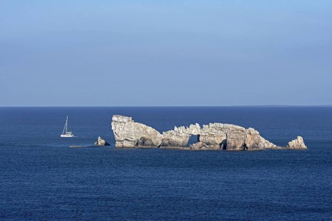 Sailing boat passing the Rocher du Lion, rock with natural arch seen from the Pointe de Pen Hir,