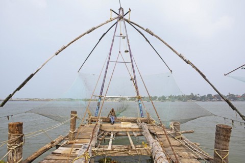 Indian fisherman sitting on a Chinese fishing net, behind him the Arabian Sea, Kochi, Kerala,